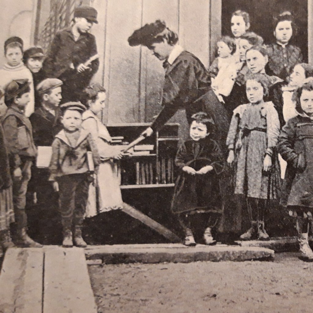 En bibliotekarie delar ut böcker till en grupp barn.