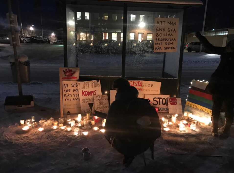 Foto på busskur med tända ljus och protestskyltar som rör flyktingars rättigheter.