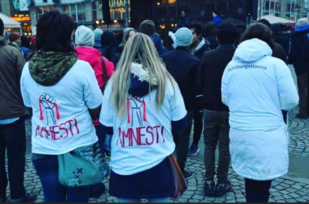 Bild på en demonstration. Två kvinnor står med tröjor som det står "Amnesti" på.