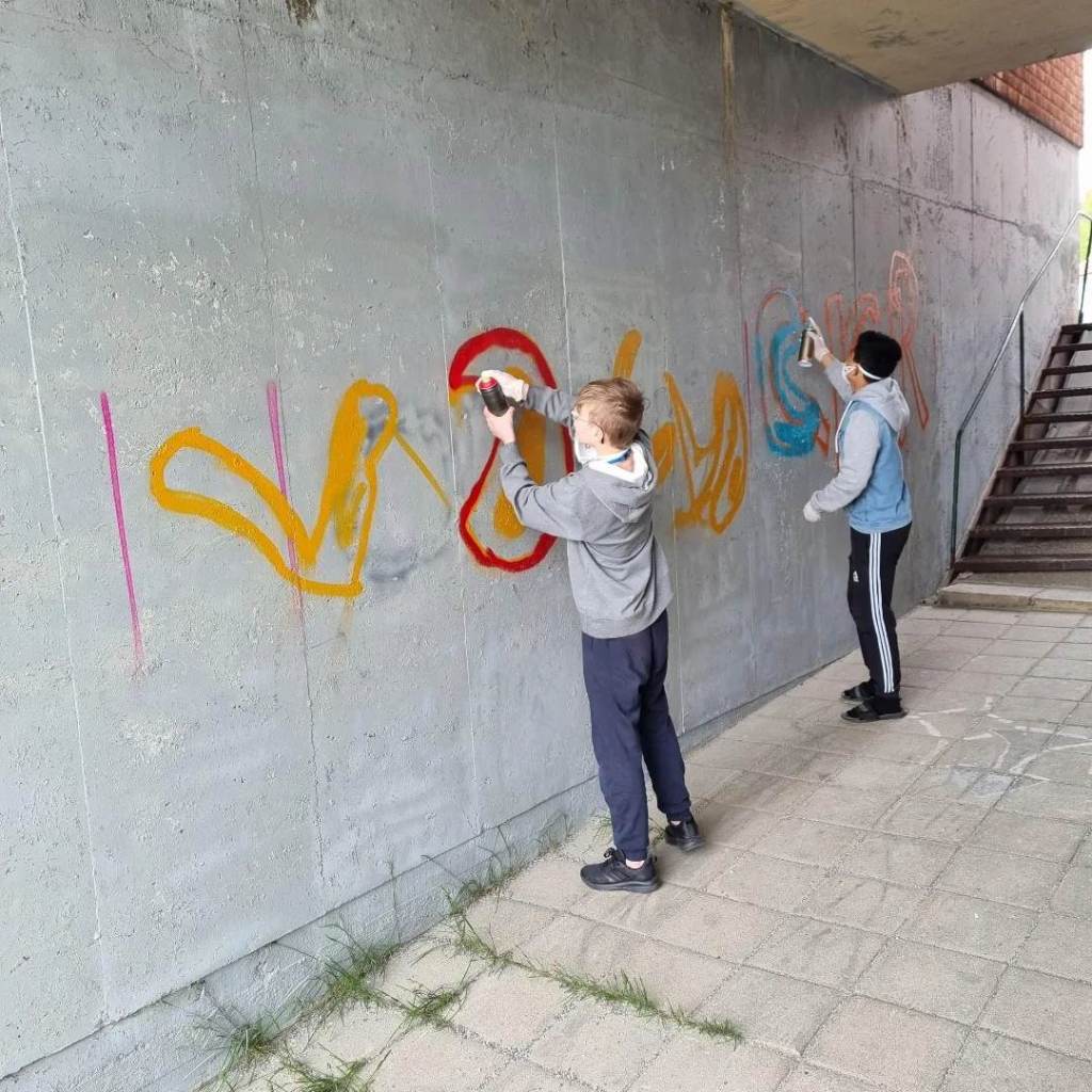 Två ungdomar som målar graffitti på en betongvägg.